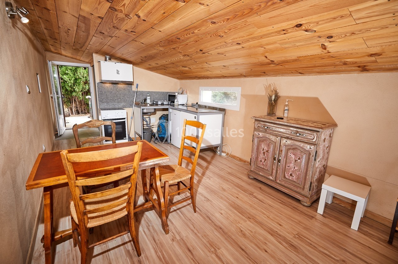 Petite pièce avec plafond en bois, coin cuisine équipé, table en bois et buffet rustique, vue sur une porte ouverte.