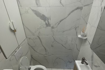 Toilettes modernes avec murs et sol en carrelage effet marbre, lavabo compact et étagères murales minimalistes.