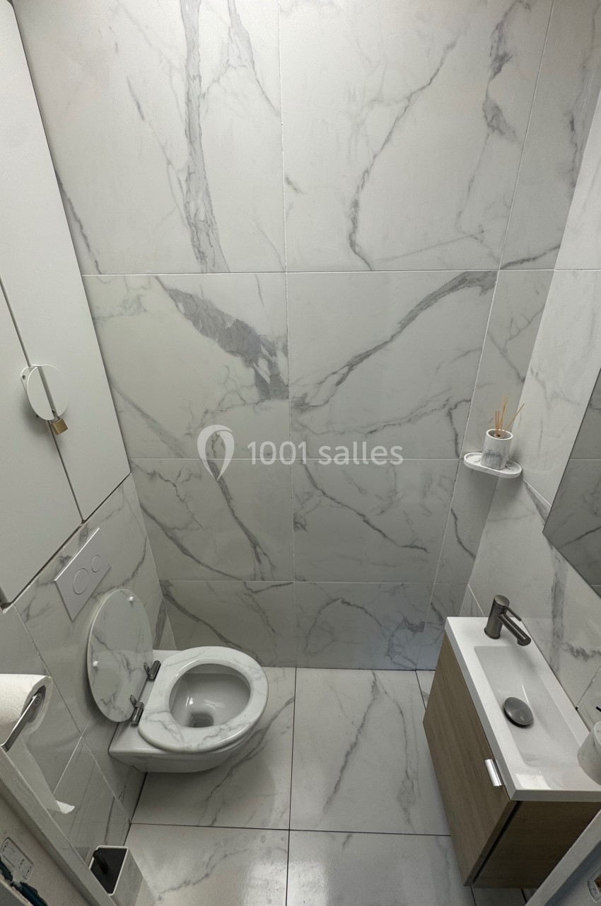 Toilettes modernes avec murs et sol en carrelage effet marbre, lavabo compact et étagères murales minimalistes.