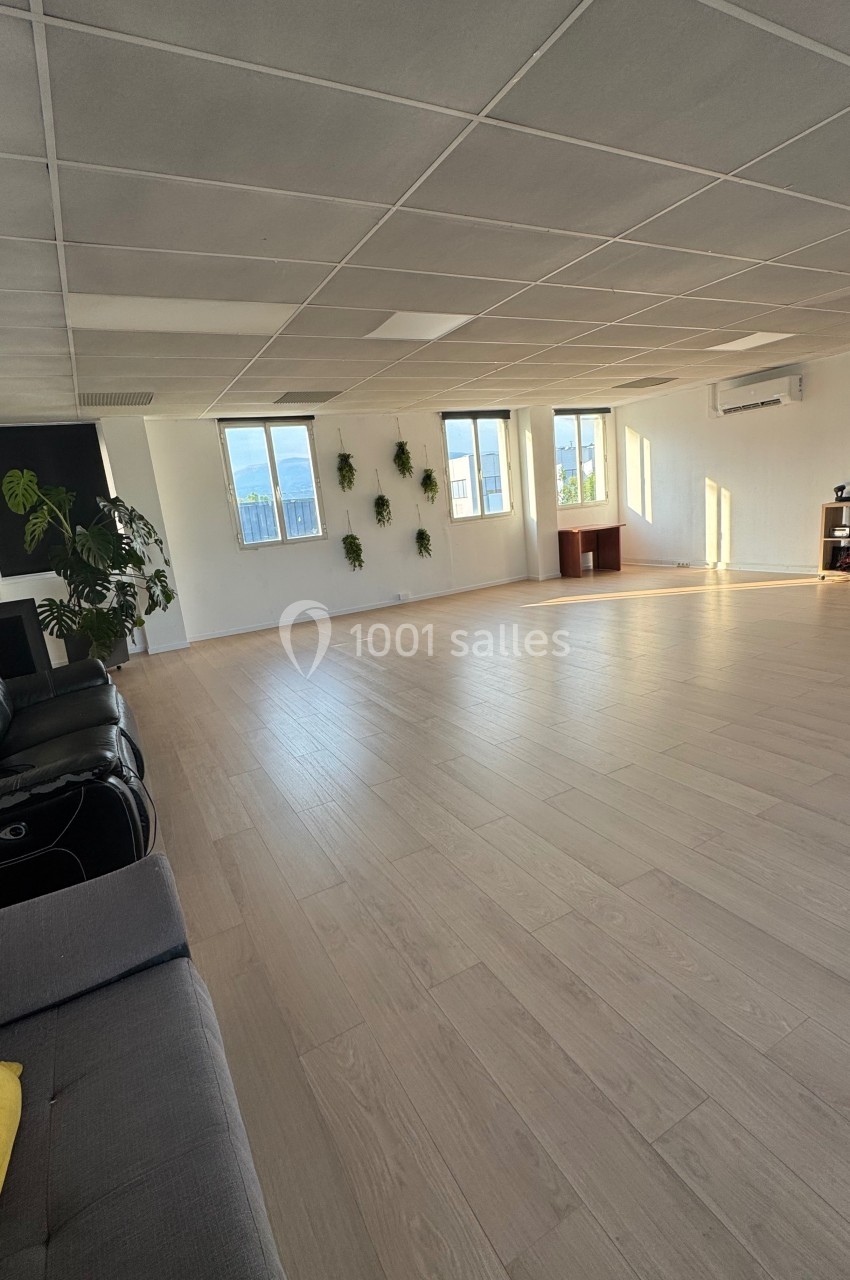 Salle lumineuse avec parquet clair, grandes fenêtres, plantes murales et quelques meubles minimalistes.