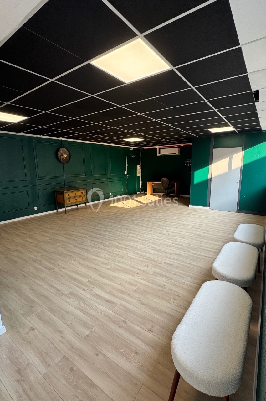 Salle vide avec parquet clair, murs verts, plafond à dalles noires, mobilier minimaliste et lumière naturelle.