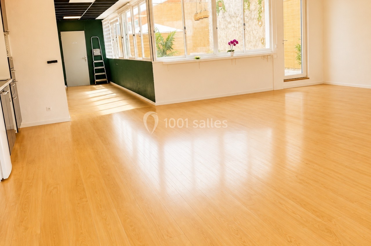 Salle lumineuse avec parquet en bois clair, grandes fenêtres donnant sur un jardin et échelle appuyée au mur.
