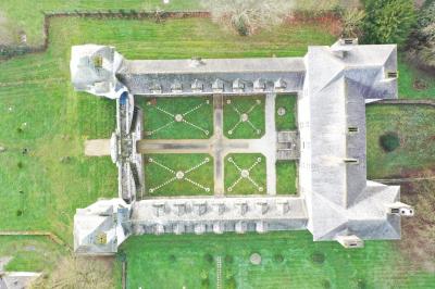 Grande salle vide avec parquet en bois, murs gris et blancs, plafond drapé de tissu beige et grandes fenêtres laissant…
