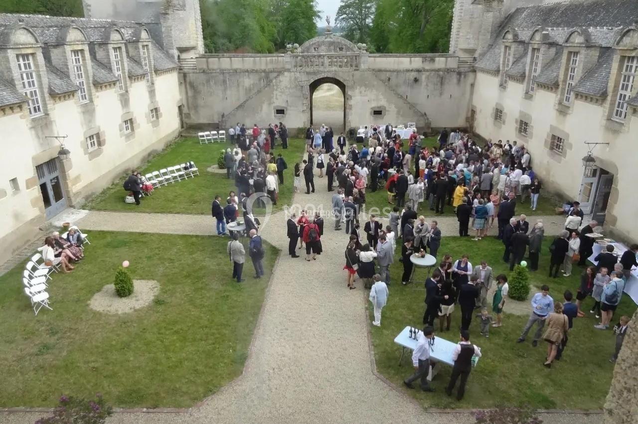 Groupe de personnes rassemblées dans la cour d'un château entourée de bâtiments anciens et d'espaces verts.