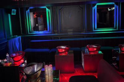 Banquettes violettes entourant des tables basses avec des seaux à champagne dans un intérieur sombre et éclairage tamisé.