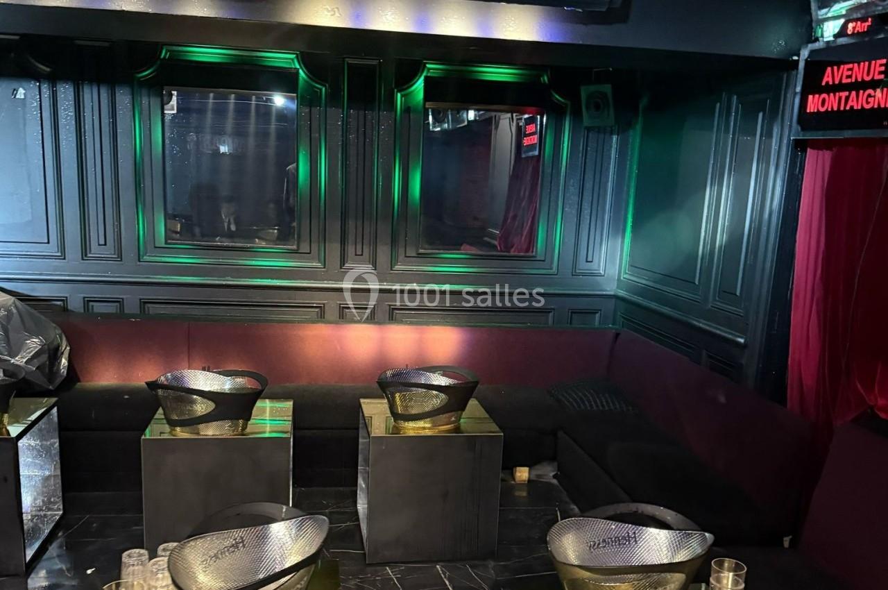 Banquettes violettes entourant des tables basses avec des seaux à champagne dans un intérieur sombre et éclairage tamisé.