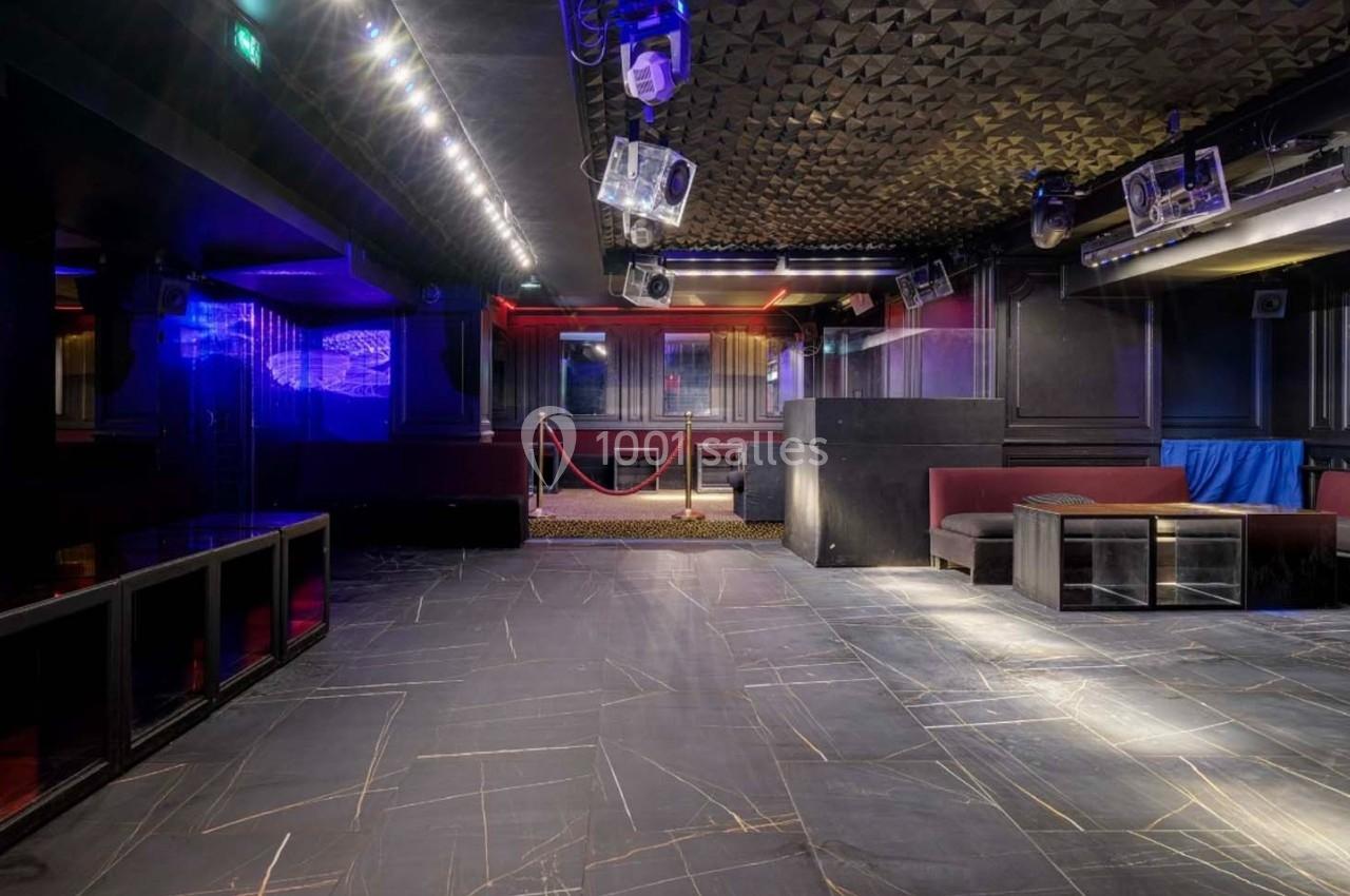 Salle de club vide avec éclairage tamisé, sol en marbre sombre, banquettes rouges et cordons de séparation.