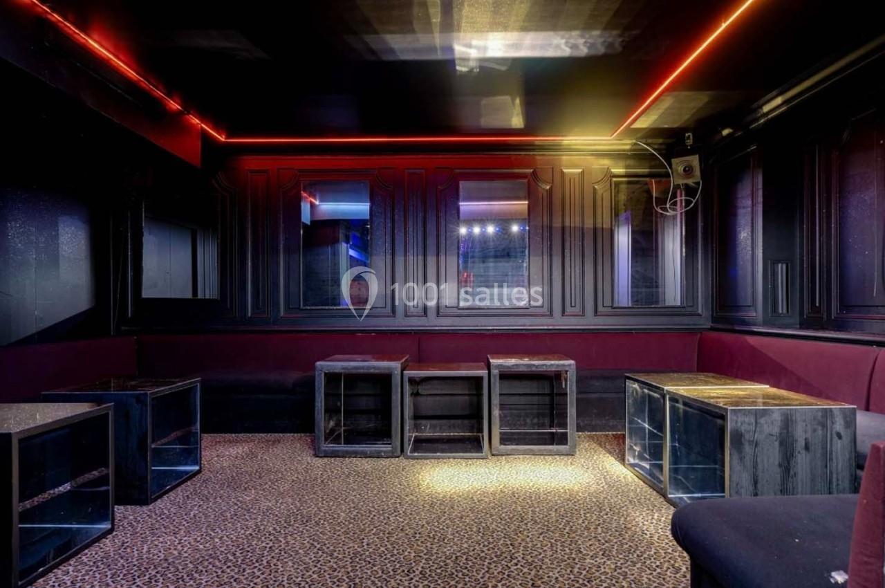 Salle sombre avec banquettes rouges, tables basses noires et éclairage tamisé aux néons rouges et jaunes.