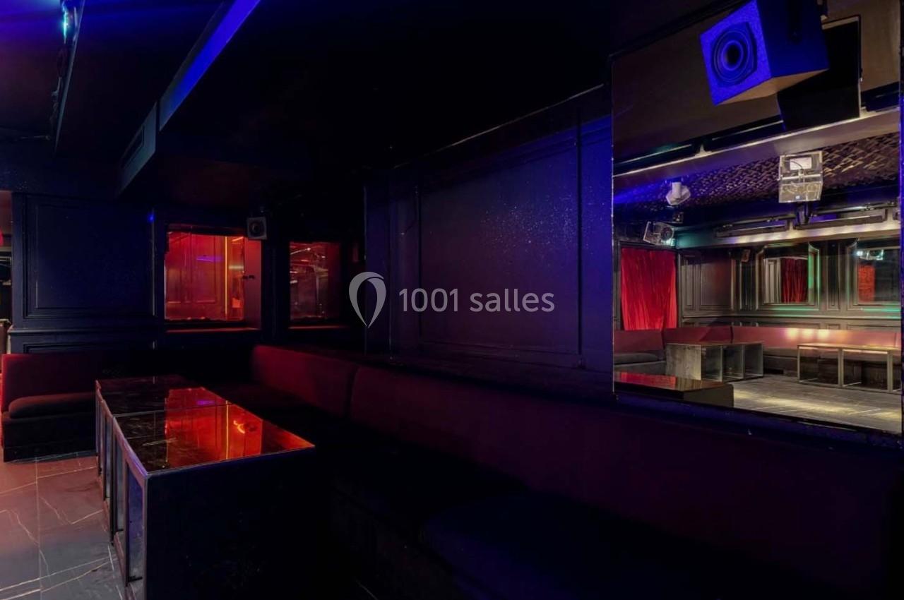 Intérieur d'une discothèque sombre avec banquettes, tables en marbre noir et éclairages rouges et bleus.