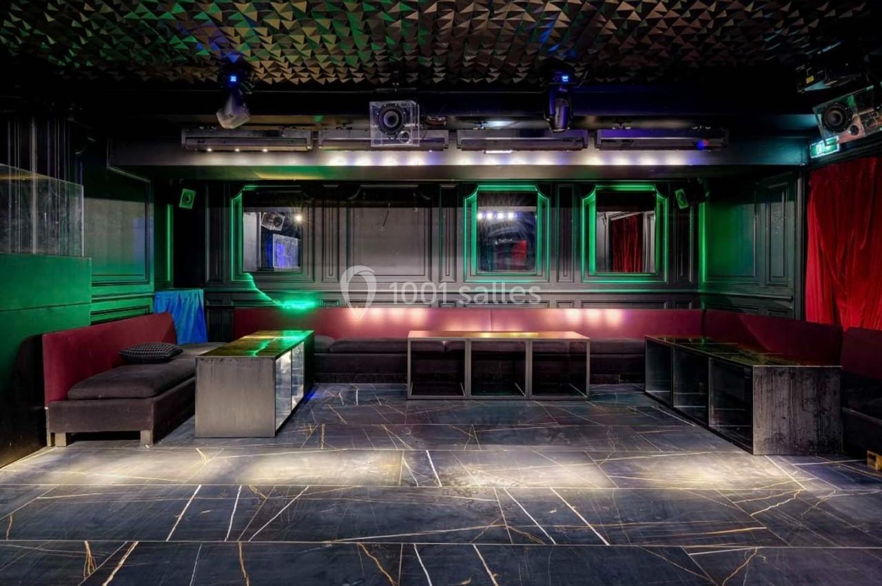 Salle de club vide avec banquettes rouges, tables basses et éclairage tamisé, sol en marbre sombre.