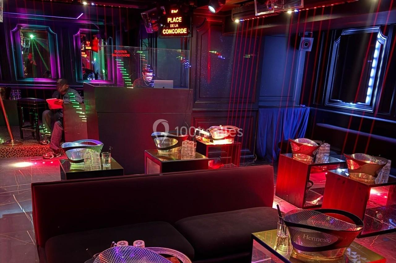 Salle de club avec banquettes, tables basses, seaux à glace et éclairage tamisé aux tons rouges et violets.