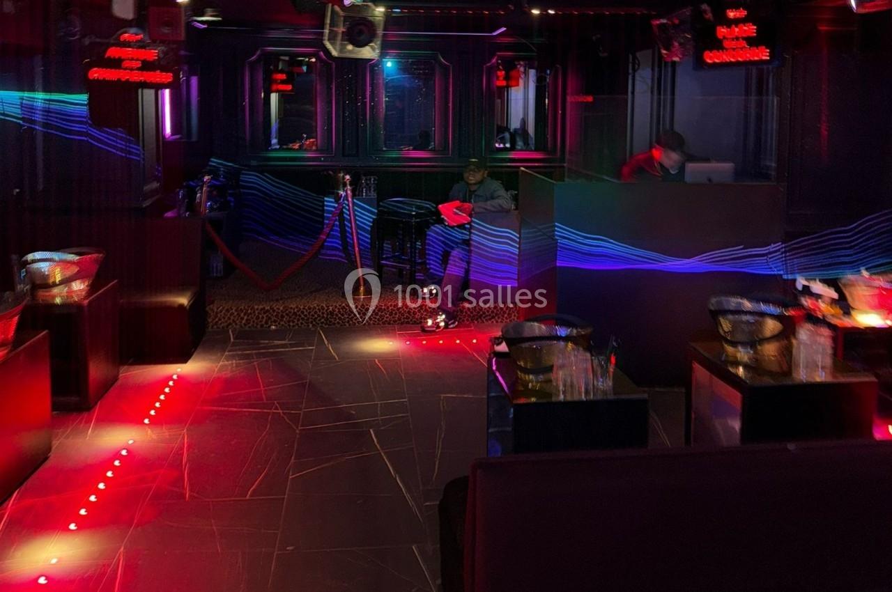 Intérieur d'une discothèque sombre avec éclairages rouges et bleus, un DJ au fond et quelques tables disposées.