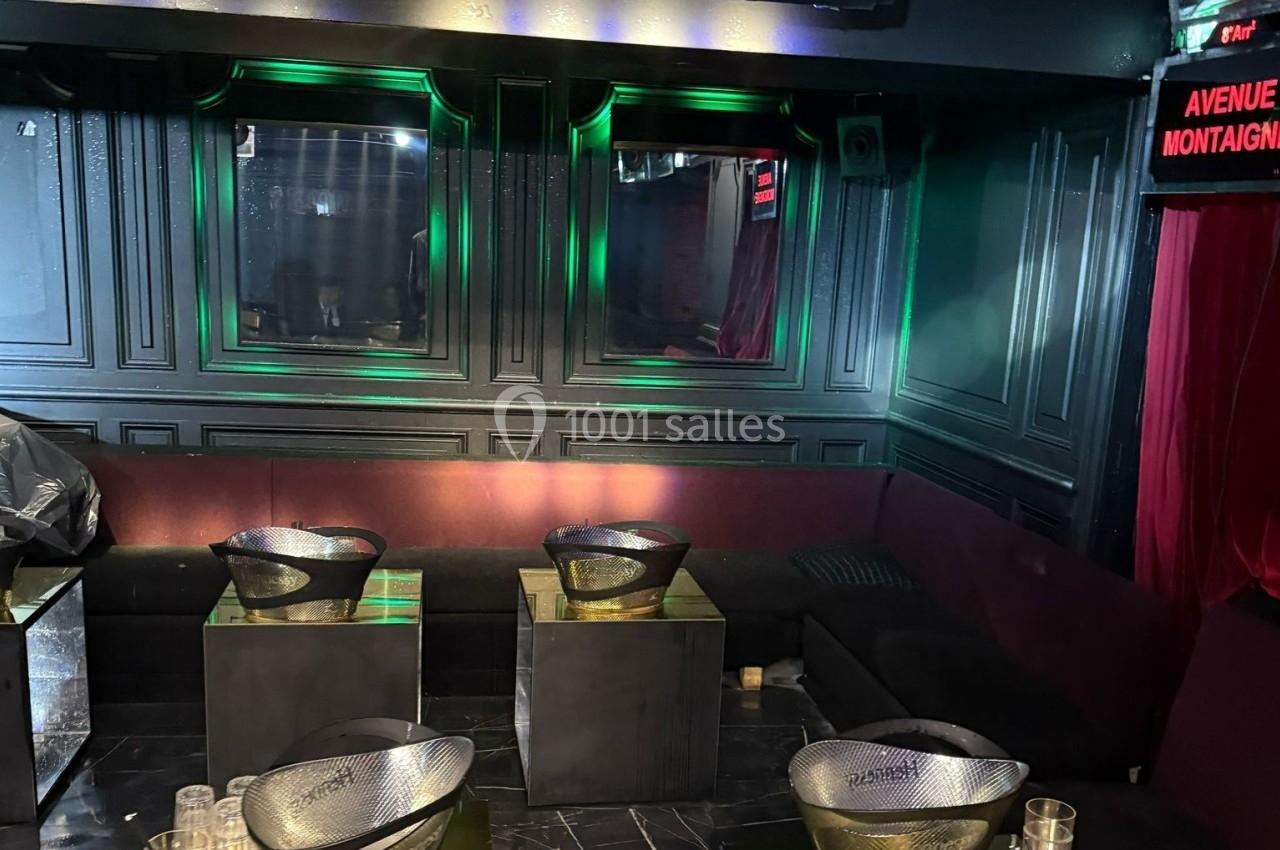 Banquettes noires et violettes entourant des tables basses avec des seaux à champagne dans un espace sombre et éclairé.