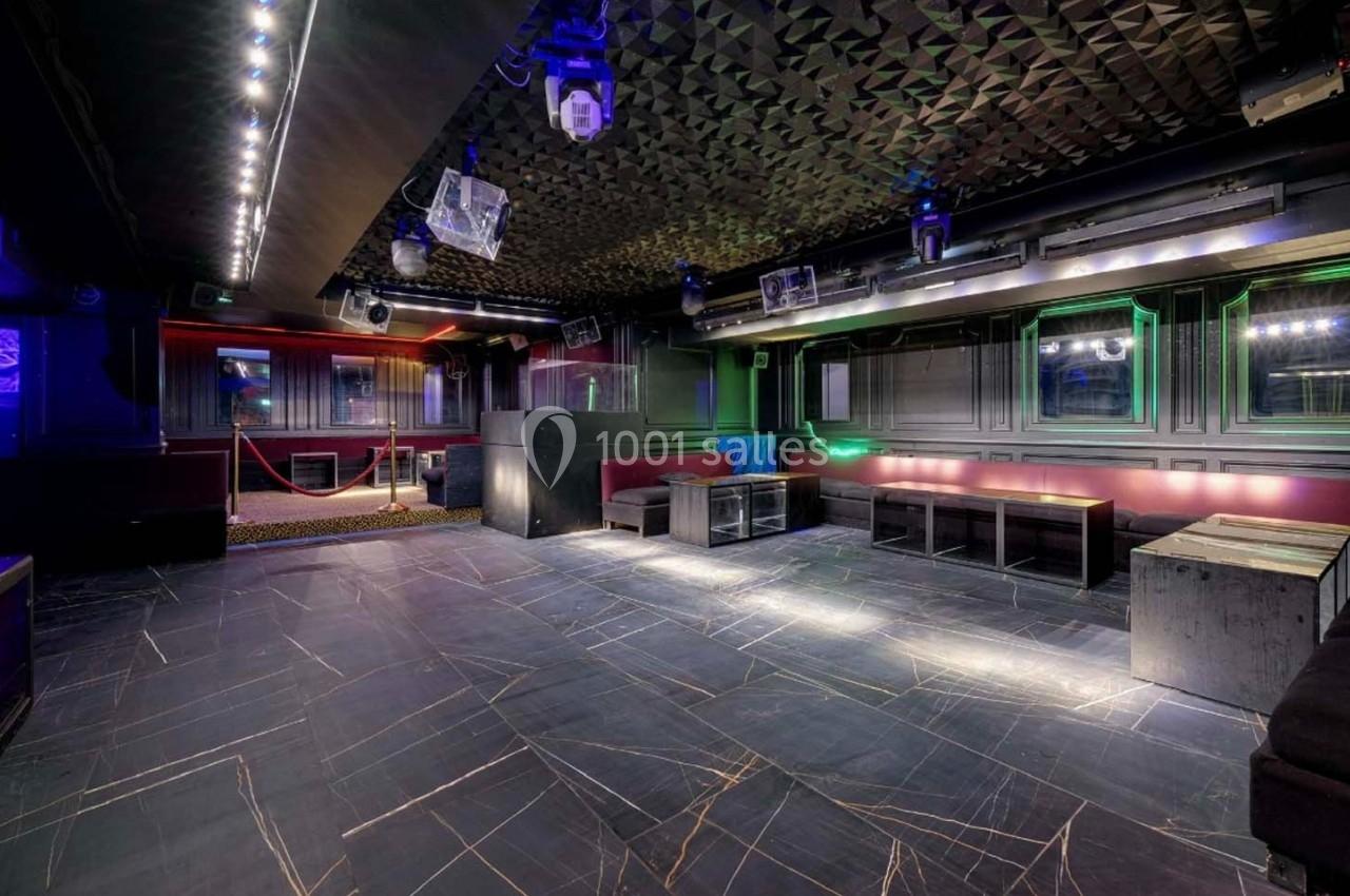 Salle de club vide avec sol en carrelage sombre, banquettes rouges et noires, éclairage tamisé et plafond texturé.