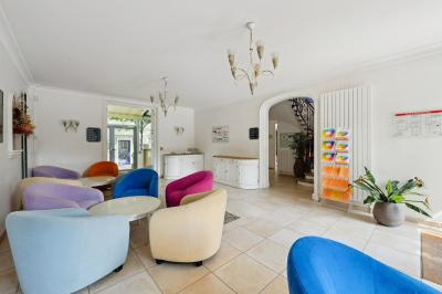 Vue d'un jardin arboré avec des tables et chaises, jouxtant un parking contenant plusieurs voitures.