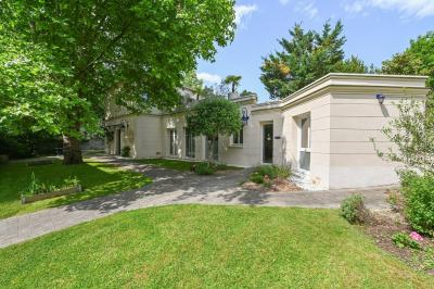 Vue d'un jardin arboré avec des tables et chaises, jouxtant un parking contenant plusieurs voitures.