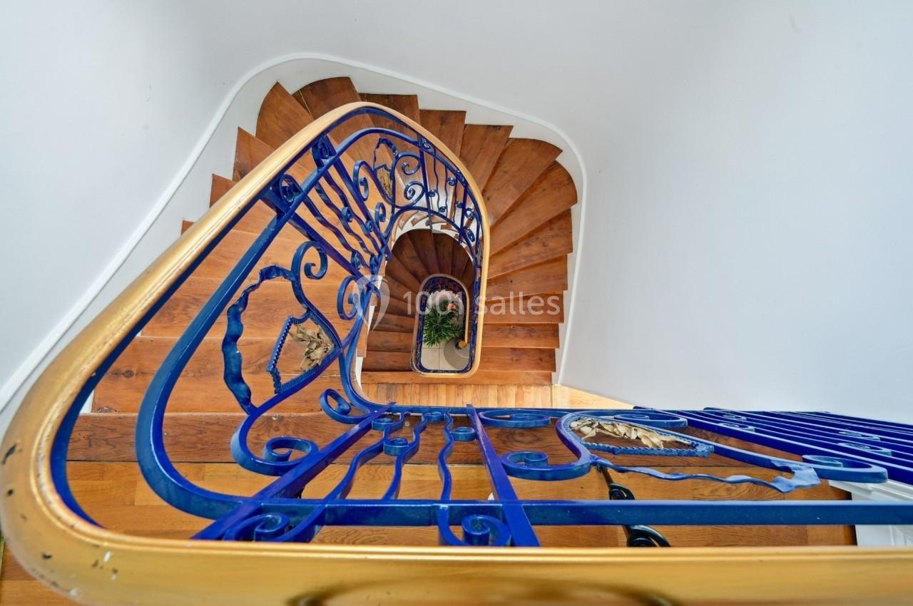 Escalier en colimaçon en bois avec une rampe en métal bleu et doré, vu en plongée depuis le haut.