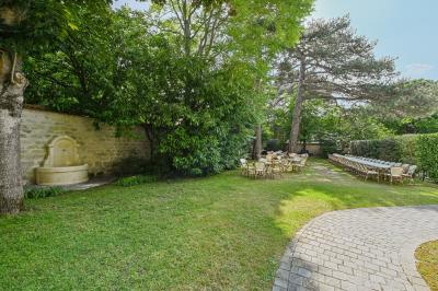 Vue d'un jardin arboré avec des tables et chaises, jouxtant un parking contenant plusieurs voitures.