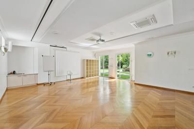 Vue d'un jardin arboré avec des tables et chaises, jouxtant un parking contenant plusieurs voitures.