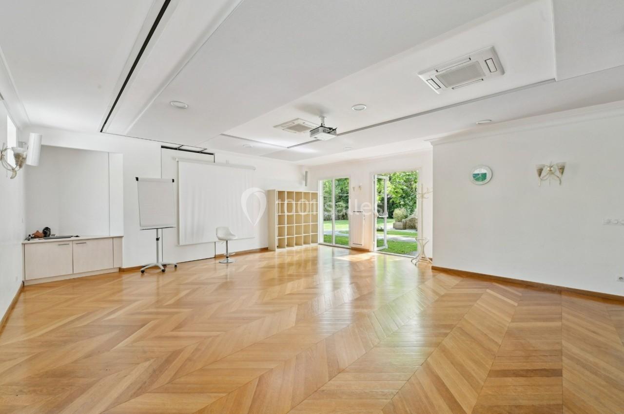 Salle lumineuse avec parquet en chevrons, murs blancs, baies vitrées donnant sur un jardin et mobilier minimaliste.