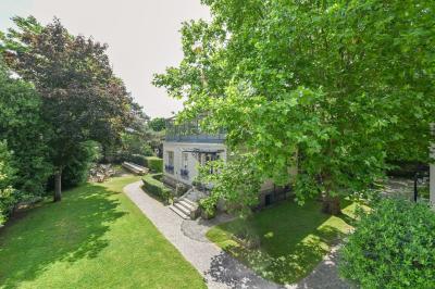 Vue d'un jardin arboré avec des tables et chaises, jouxtant un parking contenant plusieurs voitures.