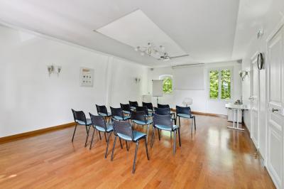 Vue d'un jardin arboré avec des tables et chaises, jouxtant un parking contenant plusieurs voitures.