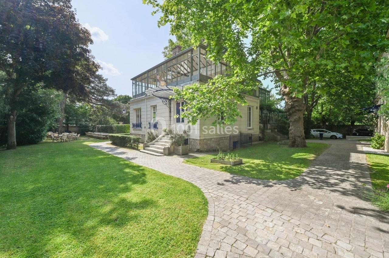 Maison en pierre avec véranda vitrée, entourée d'un jardin verdoyant et accessible par une allée pavée.