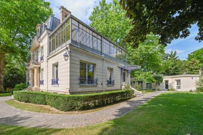 Vue d'un jardin arboré avec des tables et chaises, jouxtant un parking contenant plusieurs voitures.