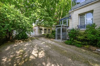 Vue d'un jardin arboré avec des tables et chaises, jouxtant un parking contenant plusieurs voitures.