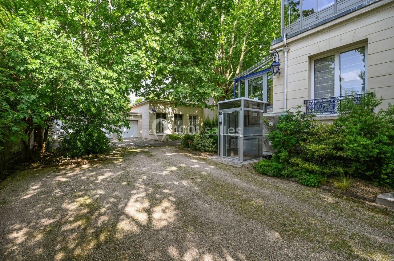 Allée gravillonnée bordée de verdure menant à une maison avec une véranda et un garage en arrière-plan.