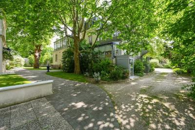 Vue d'un jardin arboré avec des tables et chaises, jouxtant un parking contenant plusieurs voitures.