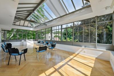 Vue d'un jardin arboré avec des tables et chaises, jouxtant un parking contenant plusieurs voitures.
