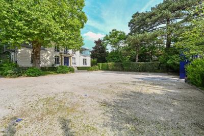 Vue d'un jardin arboré avec des tables et chaises, jouxtant un parking contenant plusieurs voitures.