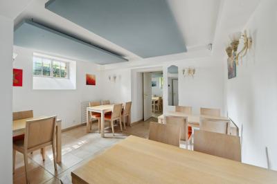 Vue d'un jardin arboré avec des tables et chaises, jouxtant un parking contenant plusieurs voitures.