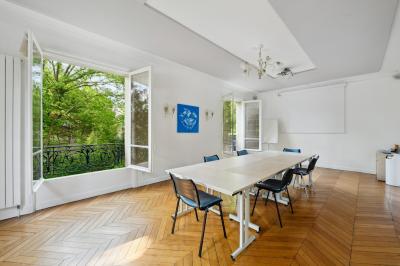 Vue d'un jardin arboré avec des tables et chaises, jouxtant un parking contenant plusieurs voitures.