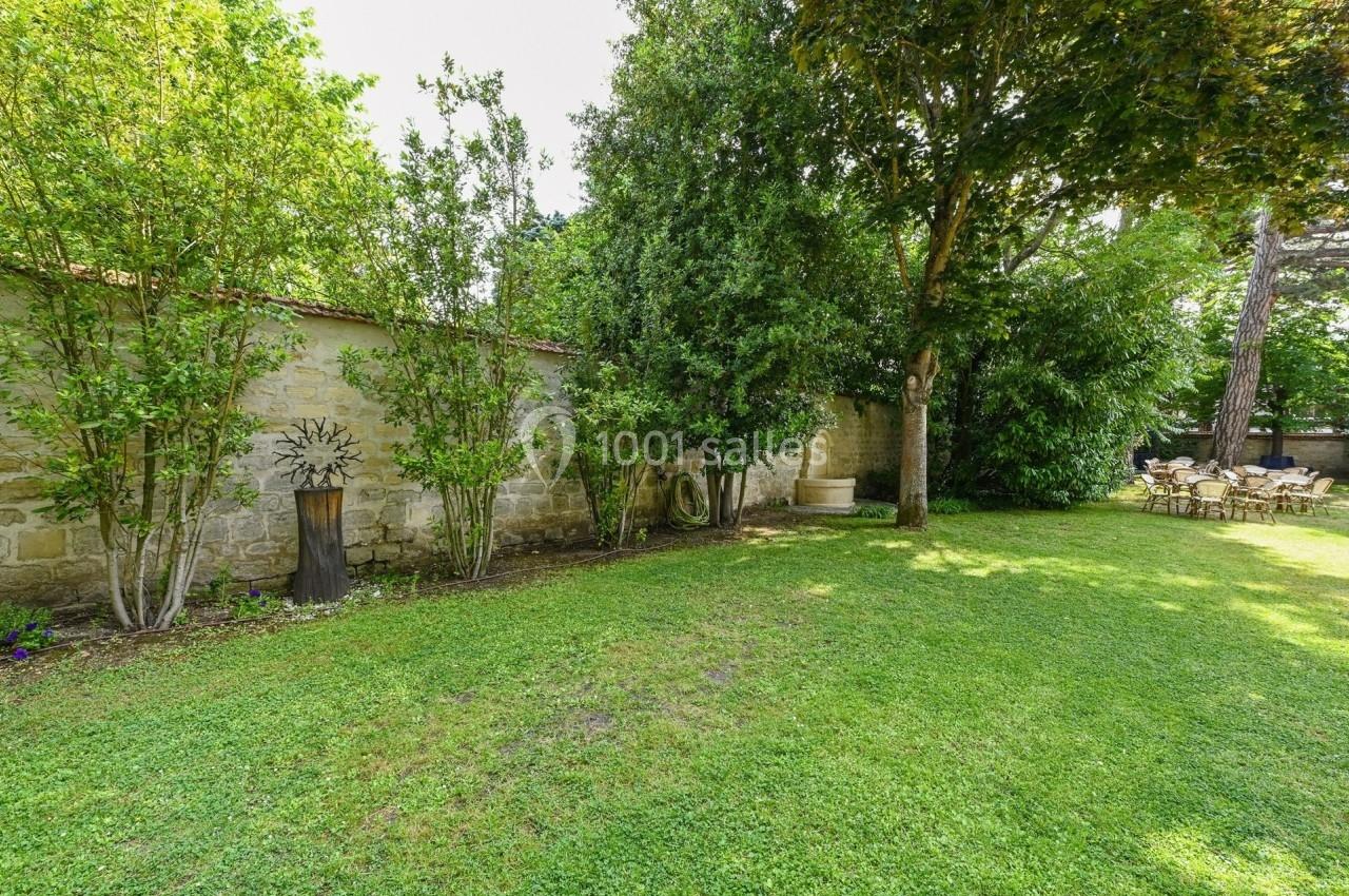 Jardin verdoyant avec pelouse, arbres, mur en pierre et une petite sculpture en métal à gauche.