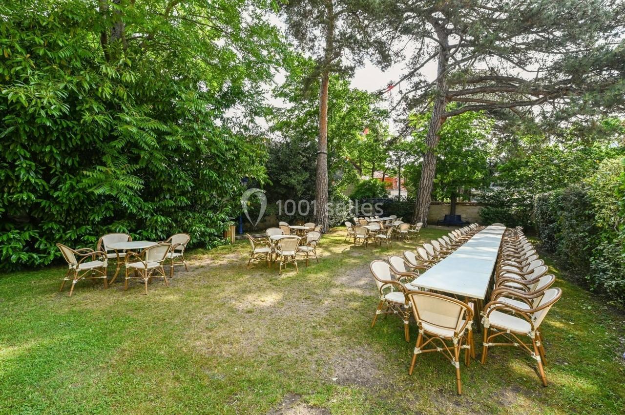 Tables et chaises disposées en extérieur sur une pelouse, entourées d'arbres et de végétation.