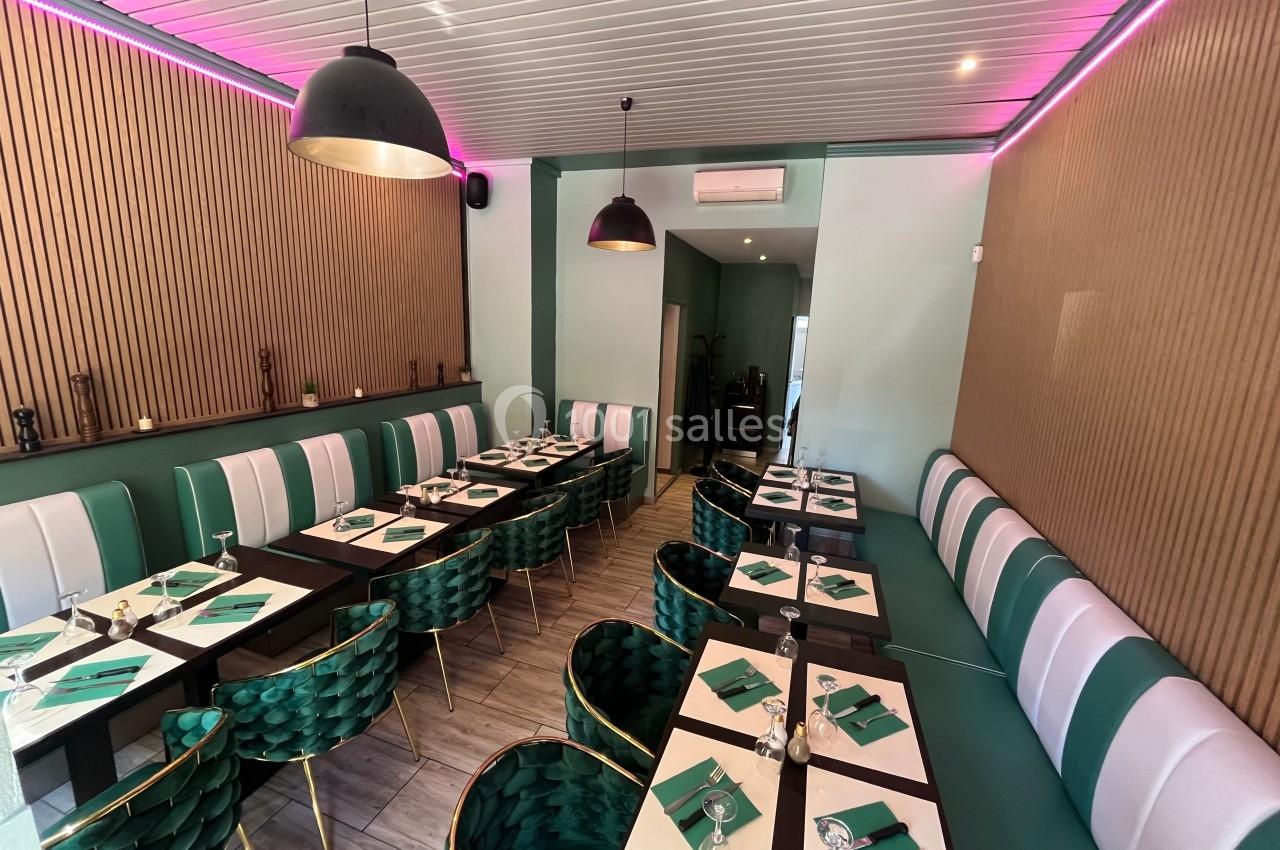 Salle de restaurant moderne avec tables dressées, chaises vertes et décoration murale en bois et néons roses.