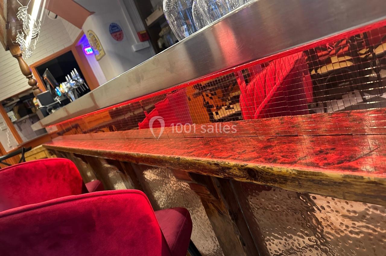 Bar en bois avec un éclairage rouge, des chaises rembourrées rouges et des bouteilles d'eau sur le comptoir.
