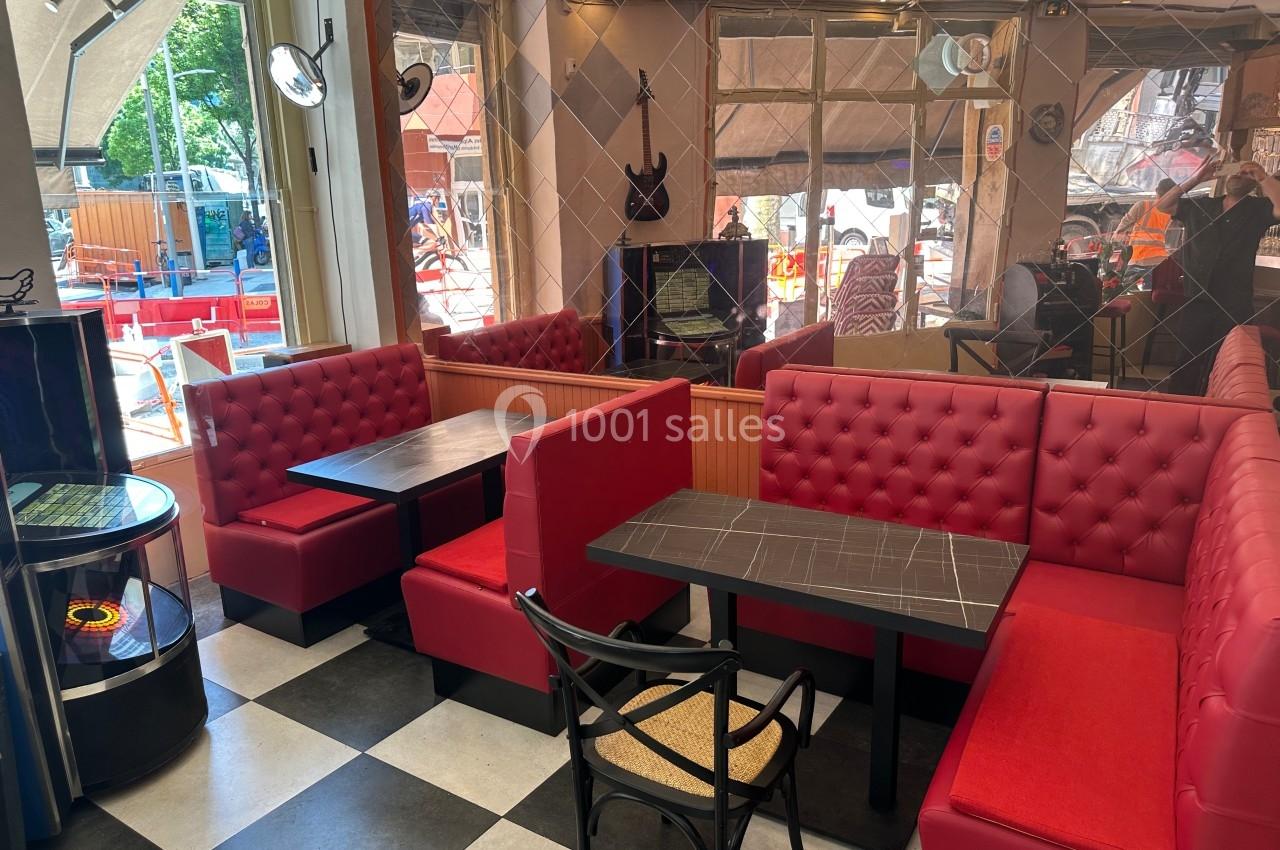 Banquettes rouges et tables noires dans un café avec sol en damier et grandes fenêtres donnant sur l'extérieur.