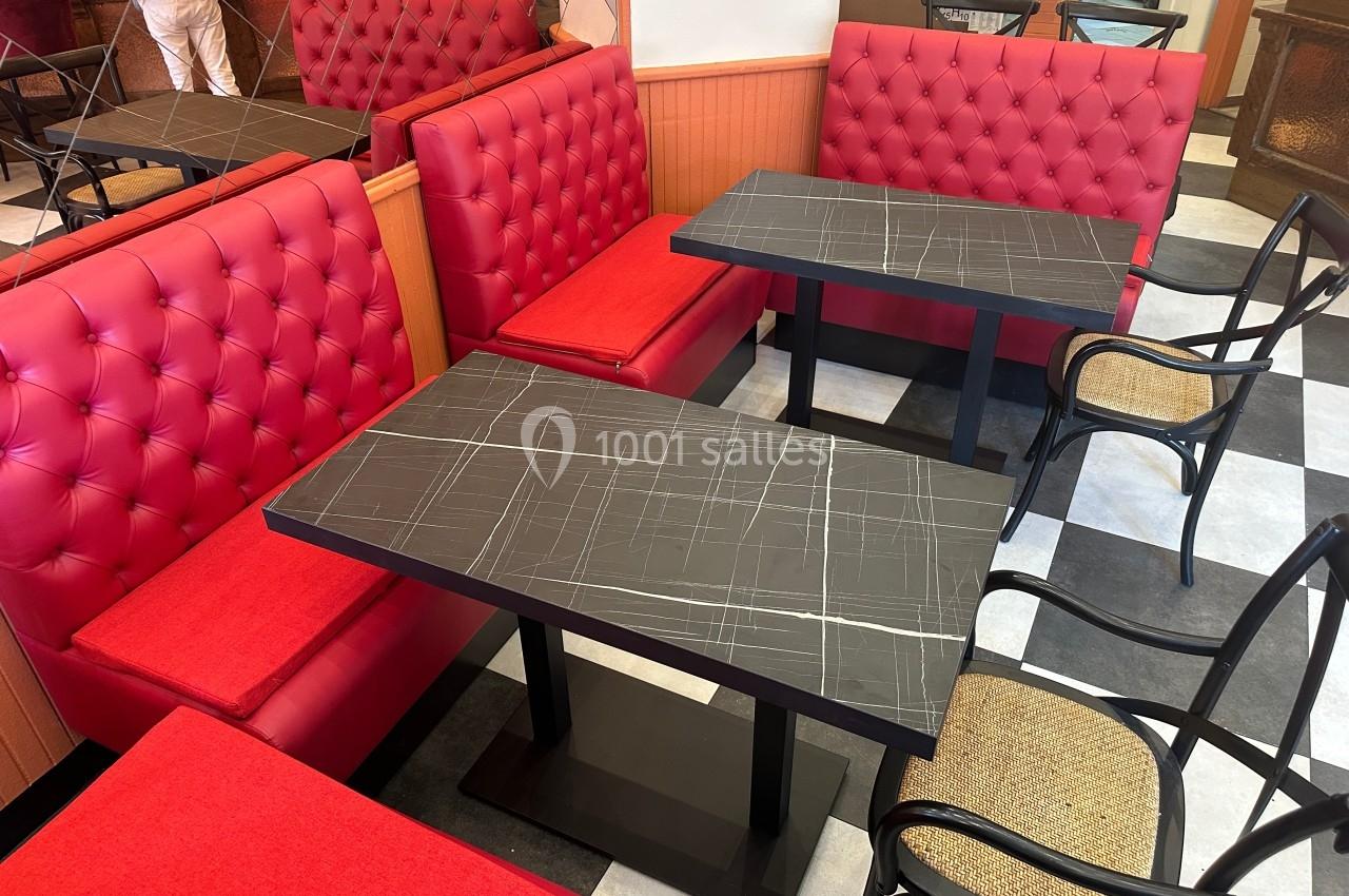Banquettes rouges et chaises en bois entourant des tables noires dans un espace de restauration au sol carrelé.
