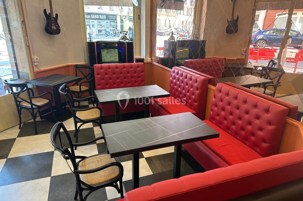 Banquettes rouges et tables noires dans un café à la décoration rétro avec guitares accrochées aux murs.