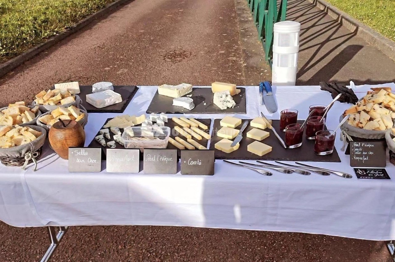 Table dressée en extérieur avec une variété de fromages, pains et confitures, accompagnés d'ustensiles et étiquettes…
