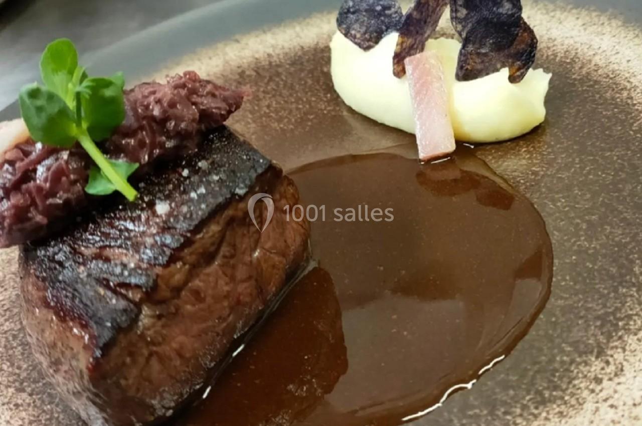 Pièce de viande grillée avec purée, chips de légumes et sauce brune sur une assiette élégante.