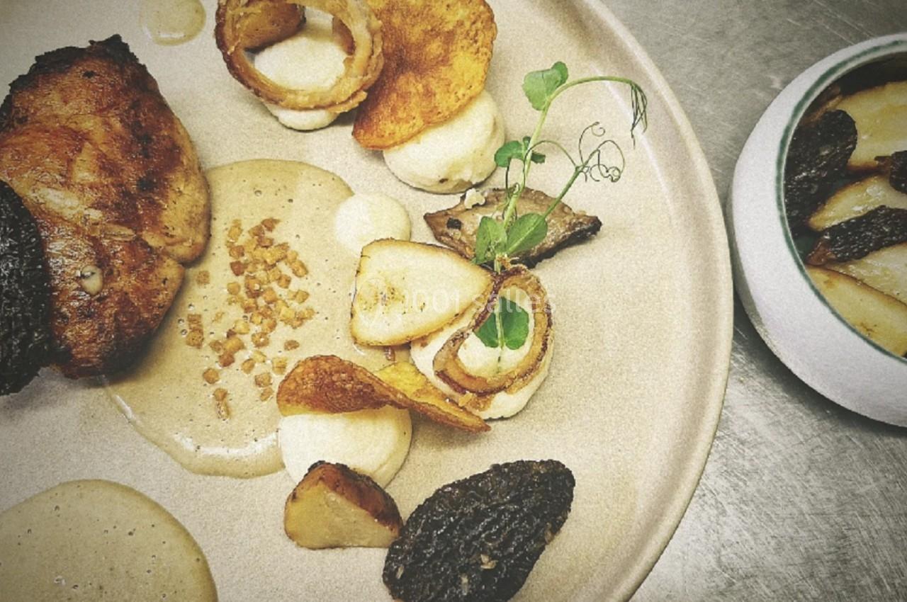 Assiette gastronomique avec viande, purée, morilles, chips de légumes et sauce, accompagnée d'un bol de garniture.