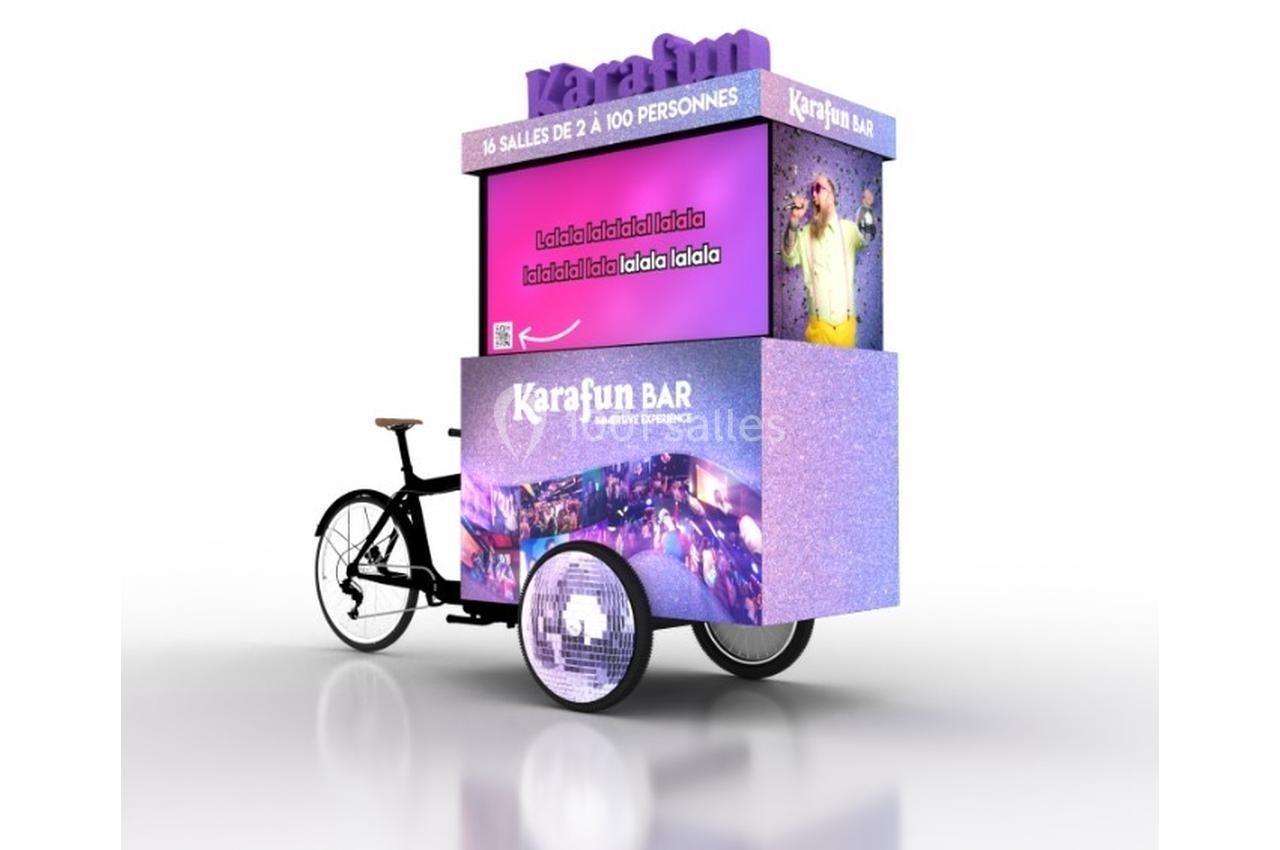 Un vélo triporteur violet avec une structure publicitaire pour un bar karaoké, affichant des images et du texte promotionnel.