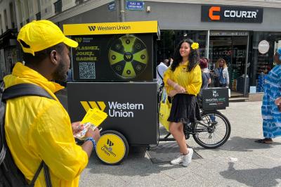 Deux personnes discutent gestuellement lors d'une soirée avec une DJ en arrière-plan et des lumières colorées.