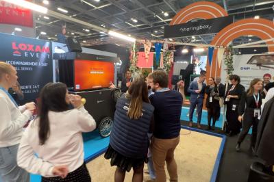 Deux personnes discutent gestuellement lors d'une soirée avec une DJ en arrière-plan et des lumières colorées.