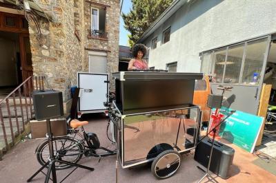 Une DJ joue de la musique sur une scène mobile montée sur un vélo, dans une cour extérieure.