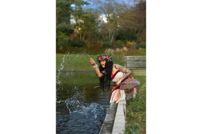 Femme en tenue traditionnelle polynésienne tenant une pagaie, devant un bar illuminé avec des flammes en arrière-plan.